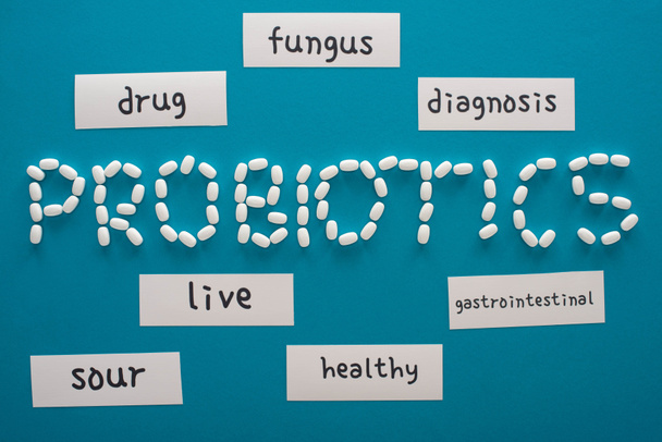 Probiyotik harflerinin üst görünümü mavi arka planda sözcüklerle kağıt kartların yanındaki haplardan yapılmıştır. - Fotoğraf, Görsel