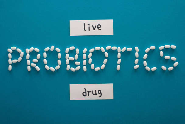horní pohled na probiotika písmo z pilulek v blízkosti papírových karet s živými a drogových slov na modrém pozadí - Fotografie, Obrázek