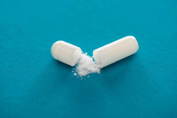 close-up zicht op probiotische capsule met wit poeder op blauwe achtergrond - Foto, afbeelding