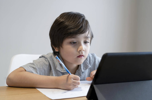 Kid Selbstisolierung mit Tablet für seine Hausaufgaben, Kind mit digitalem Tablet, das Informationen im Internet sucht, während covid-19 Lock-Down, Social Distancing, E-Learning und Online-Bildung - Foto, Bild