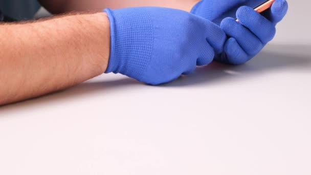 mãos masculinas em luvas azuis substitui um protetor de tela de vidro temperado quebrado para um smartphone. Um homem prepara um smartphone para substituir o vidro. Conceito de reparação Smartphone. espaço de cópia
 - Filmagem, Vídeo