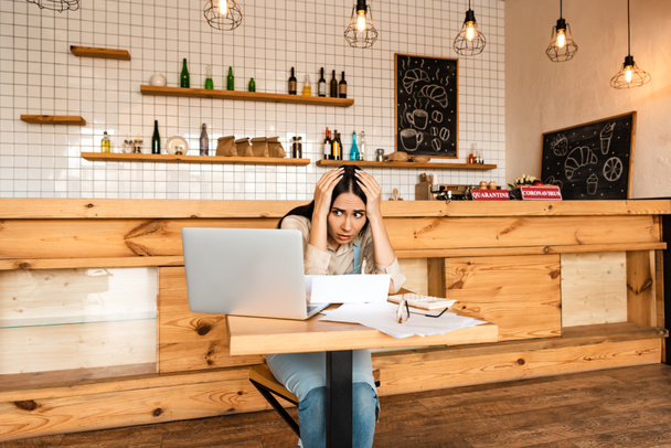 Stressed cafe owner looking at laptop near documents at table - Photo, Image