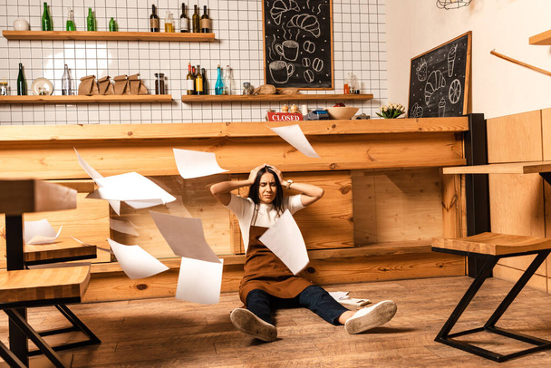 Propriétaire de café stressé avec les yeux fermés près de la table et des papiers autour sur le sol
 - Photo, image
