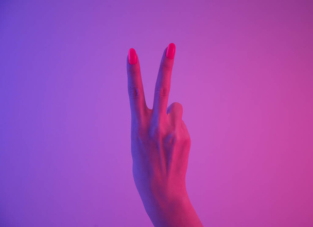 Female hand with vivid orange manicure showing peace sign gesture in neon pink light. - Photo, Image