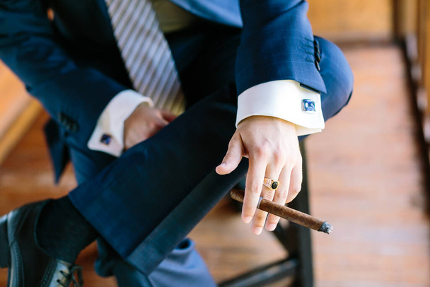 big boss style, masculinity concept. close-up of the hand of a young businessman smoking cigar and sitting on a chair. - Foto, Imagem