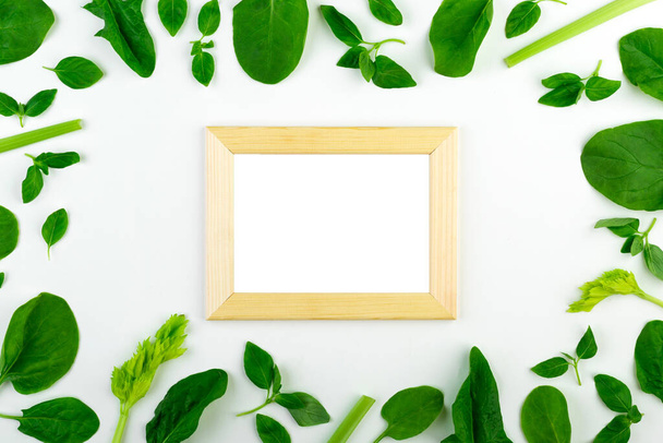 Fresh green vegetables and herbs set on a white background around an empty frame.  - 写真・画像