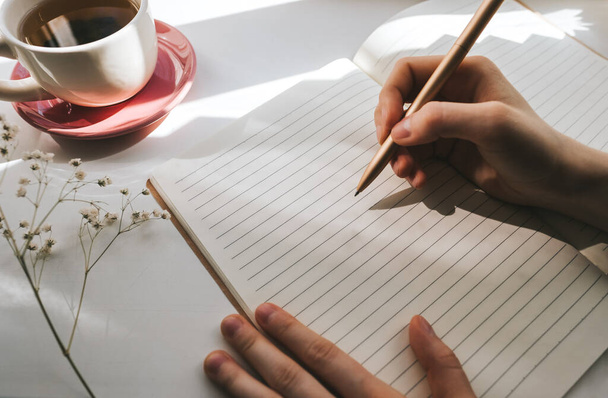 Γυναίκα πίνοντας τσάι και κρατά σημειώσεις σε ένα σημειωματάριο. - Φωτογραφία, εικόνα
