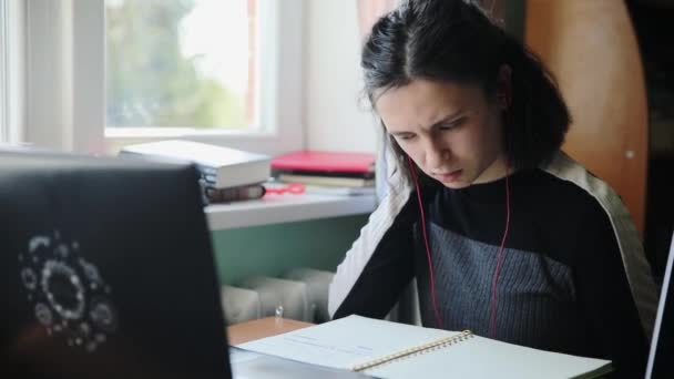 Молодая белая девушка в черном свитере смотрит на блокнот, когда учится дома.
  - Кадры, видео