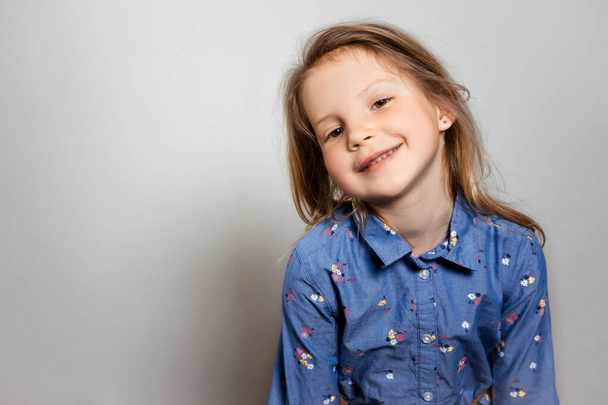 Retrato de niña bastante sonriente en vestido azul sobre fondo gris aislado
.  - Foto, Imagen