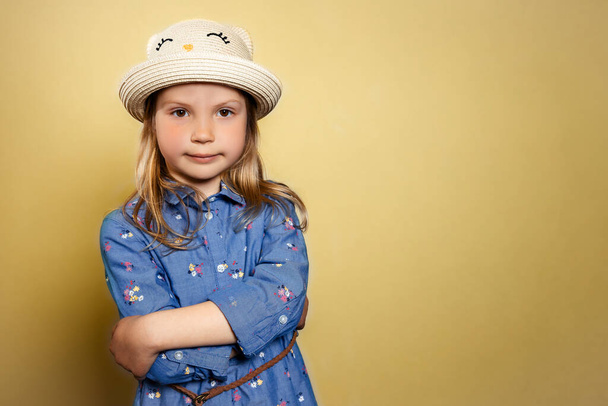 Portret van mooi klein meisje in blauwe jurk en gele hoed op gele geïsoleerde achtergrond.  - Foto, afbeelding