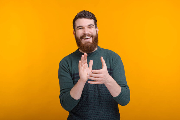 Cheerful smiling man is applausing on yellow background. - Photo, Image