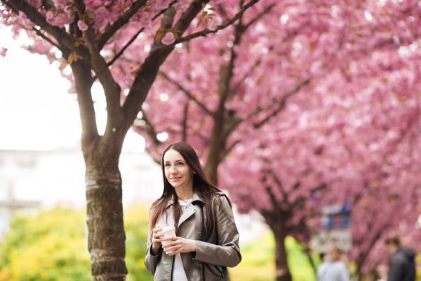 Womens beauty and fashion. Urban lifestyle. girl on the background of pink flowering trees. Closeup portrait of girl in spring - Photo, Image
