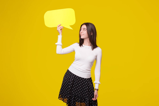 Pretty young woman is holding up a bubble speech on yellow background. - Fotografie, Obrázek