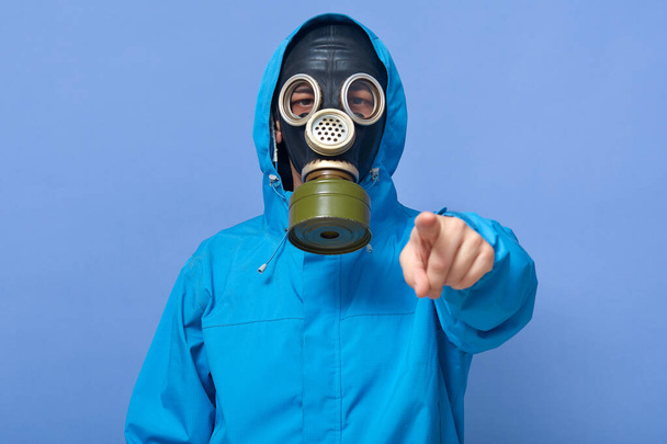 Closeup portrait of ecologist frights with factories which pollute air, water, forests and land, scientist wearing uniform and respirator, pointing to camera with with fore finger against blue wall. - Foto, Bild