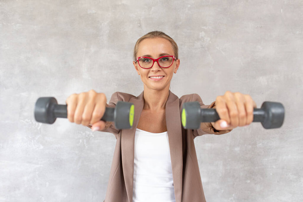 Charming blond woman holds dumbbells in hands in front of herself. Selective focus - Fotografie, Obrázek