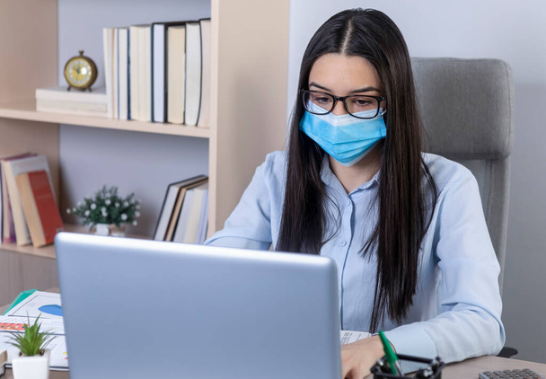 Coronavirus salgını sırasında ofiste çalışan yüzü maskeli bir iş kadını. Pandemik konsept sırasında evde çalışmak. - Fotoğraf, Görsel