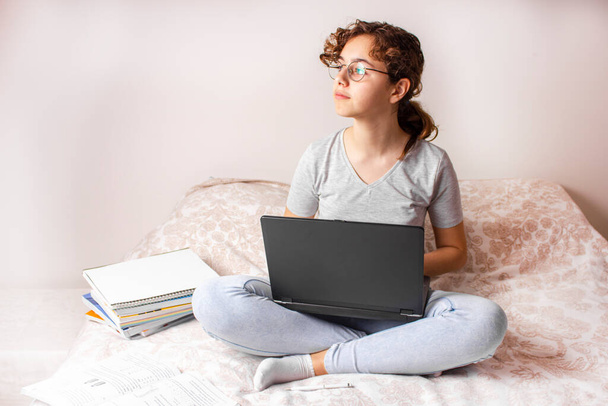Έφηβος κορίτσι σπουδάζει στο κρεβάτι στον υπολογιστή και ψάχνει για παράθυρο - Φωτογραφία, εικόνα
