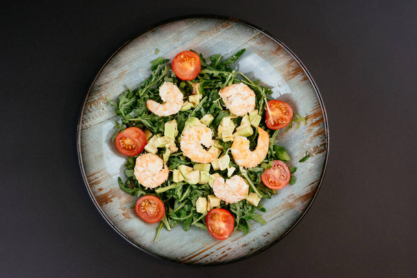 Salat mit Garnelen und Tomaten auf blauem Teller auf schwarzem Hintergrund - Foto, Bild