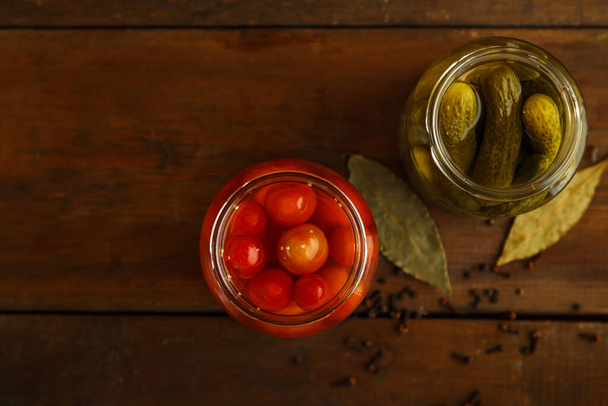 Jars of pickled cucumbers and homemade pickled tomatoes on a linen towel on a wooden table - Fotó, kép