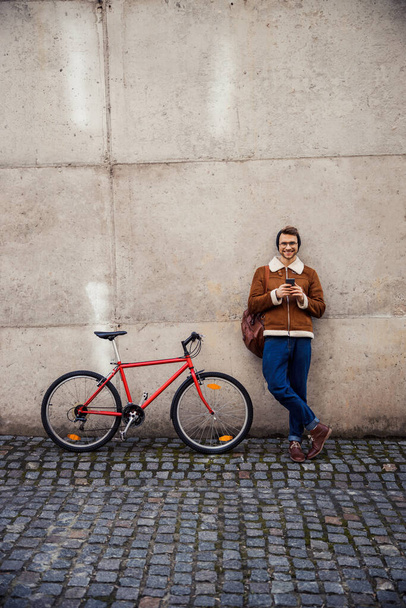 Mirthful cyclist relaxing by the wall outdoors and smiling - Fotó, kép