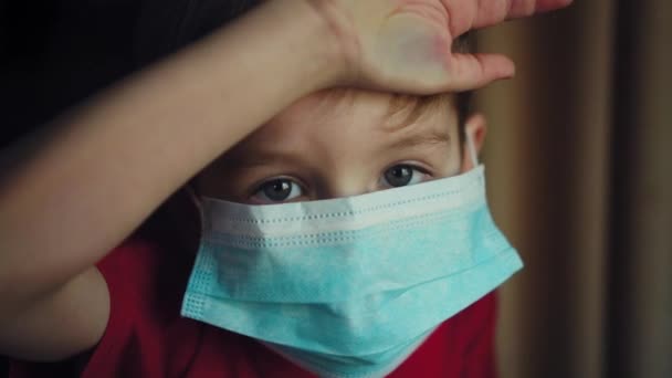 Jonge jongen met een medisch masker kijkt uit het raam. isolatie in quarantaine, coronavirus, covid 19. - Video