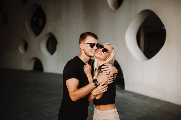 Serious couple in the city at daylight guy hugging and kissing blonde lady on the cheek. Outdoor street fashion photoshoot of newly wed freelance couple. - Photo, Image