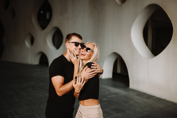 Serious couple in the city at daylight holding hands with amazing building white wall facade background. Outdoor street fashion photoshoot portrait. - Photo, Image