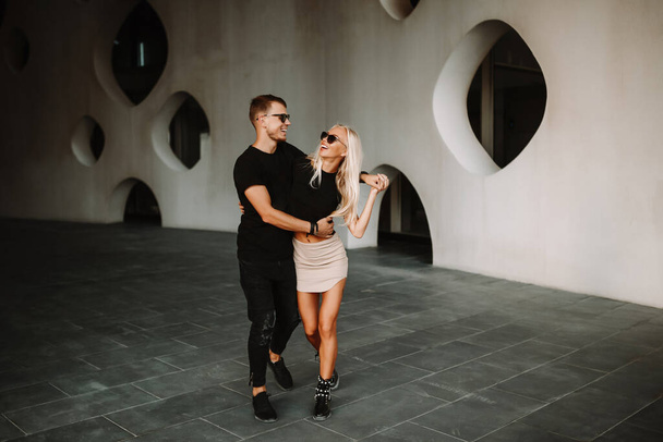Charming passionate freelance couple enjoying time outdoor with sweet talk and hugging in the public. Street fashion photoshoot in white wall building facade. - Photo, Image