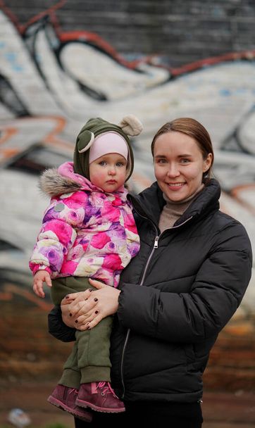 Красива молода мама з милою дочкою в барвистій куртці з капюшоном на дитячому майданчику навесні. Концепція щасливої сім'ї та весни
 - Фото, зображення
