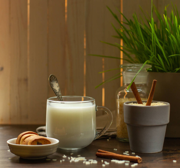 Rice vegetable milk in a glass Cup and crackers in a saucer on a wooden table with sticks and cinnamon and rice grains, blurred background - Photo, image
