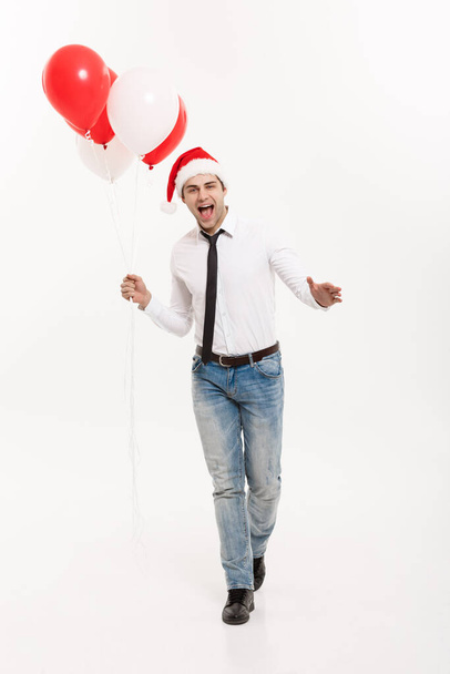 Concepto de Navidad - Guapo hombre de negocios feliz caminando con globo rojo celebrar feliz Navidad y feliz año nuevo usar sombrero de santa
. - Foto, Imagen