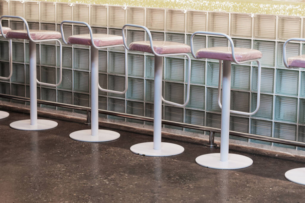 View of a row of bar stools that stand near a bar counter made of glass blocks. Concept interior, business, quarantine - Zdjęcie, obraz