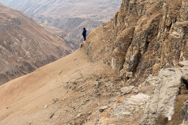 Egy lány kék kabátban és bordó farmerben áll a hegy szélén egy homokos kanyonban. Fogalom emberek, táj, utazás - Fotó, kép