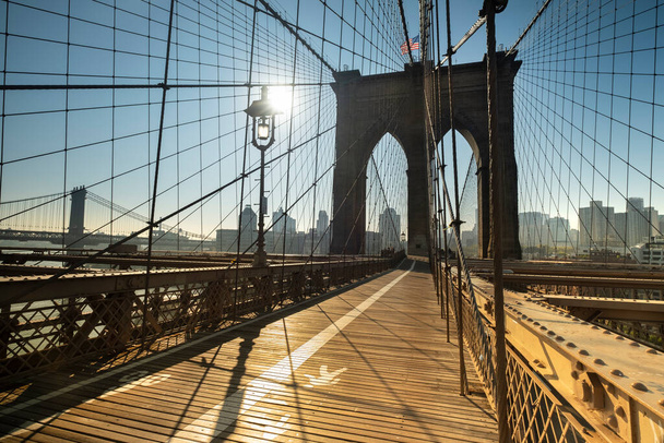 Vroege ochtendzon komt op op het pad van de Brooklyn Bridge over de East River tussen Manhattan New York en Brooklyn USA - Foto, afbeelding
