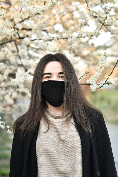 Tyttö lääketieteellisessä naamiossa ja käsineet taustalla kukkia COVID-19, kevät valkoinen
. - Valokuva, kuva