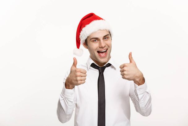 クリスマスのコンセプト-ハンサムなビジネスマンは白い隔離された背景でthumpを示すサンタの帽子を身に着けています. - 写真・画像
