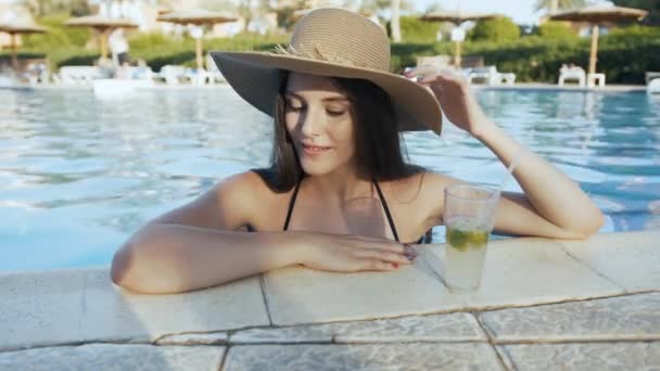 Woman in hat relaxing at pool with cosmopolitan cocktail - Felvétel, videó