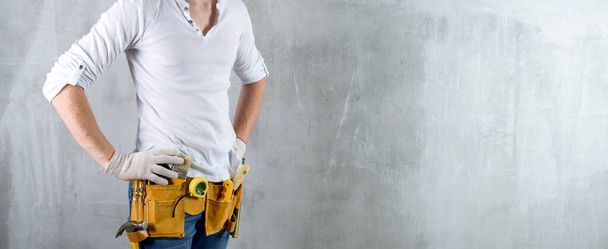 Builder worker engineer in a white shirt with an installer belt close up, space for text on a concrete wall handyman tool diy - Photo, image