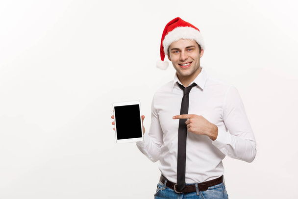 クリスマスのコンセプト-ハンサムなビジネスマンは、モバイル画面上で何かを提示陽気なクリスマスを祝い、幸せな新年はサンタの帽子を着用. - 写真・画像