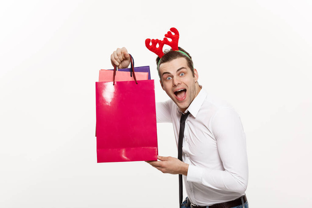 Noel Konsepti - Yakışıklı İş adamı mutlu noeller ve mutlu yıllar kutluyor Ren geyiği saç bandı takıyor ve Noel Baba 'nın kırmızı büyük çantasını tutuyor. - Fotoğraf, Görsel
