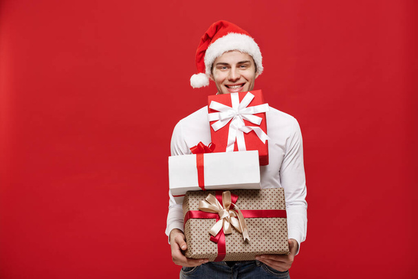 Kerst Concept - Knappe blanke gelukkig zakenman met veel geschenken met slijtage santa hoed poseren op witte geïsoleerde achtergrond. - Foto, afbeelding