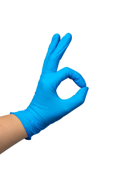 La main de la femme dans des gants de caoutchouc chirurgicaux bleus faisant OK signe isolé sur un fond blanc. Chemin de coupe inclus. - Photo, image
