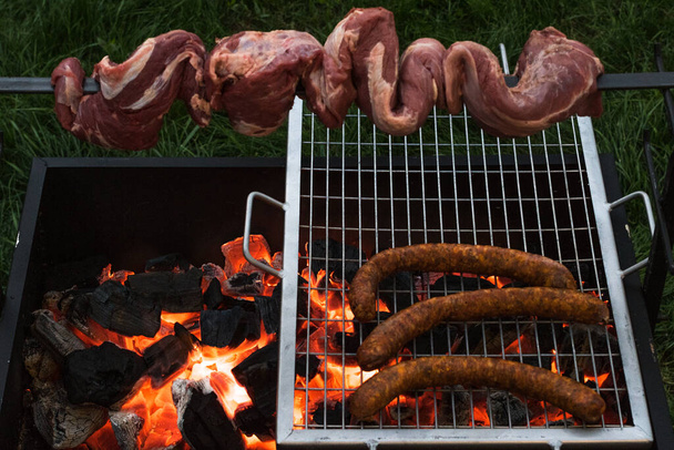 Barbecue with beef inserted in a sword and some sausages on a charcoal grill - Photo, Image
