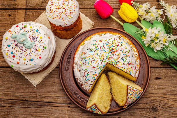 Easter cakes on old wooden table. Traditional Orthodox festive bread, cut pieces, artificial decor - Фото, изображение