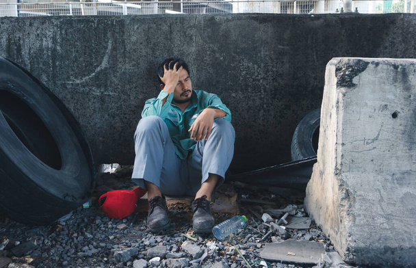 Un sans-abri asiatique est assis près du mur. Son visage est plein de souffrance, de dépression et de désespoir. Les gens sont au chômage en raison des effets de l'épidémie du virus de la couronne
. - Photo, image