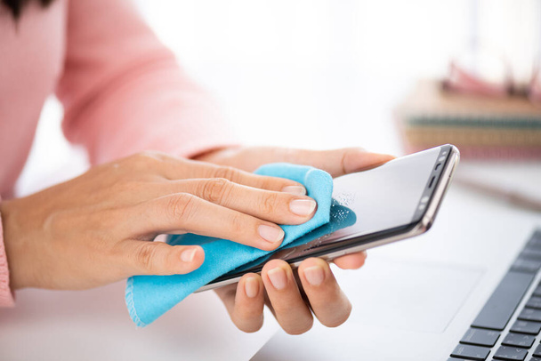 Closeup woman hands cleaning the smartphone screen with a fiber cloth from dirt dust and virus, against Coronavirus or Corona virus disease (Covid-19). Healthcare and disinfection concept. - Photo, image