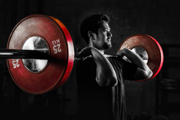 asian athletic strong man having workout and bodybuilding with barbells weightlifting front squat style in gym and fitness center in dark tone two tone - Fotoğraf, Görsel