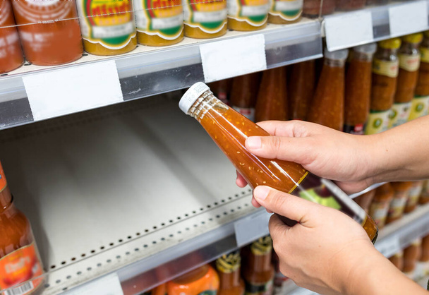 BANGKOK, THAILAND- MARCH 15 2020: Woman hand holding ketchup bottle and Empty shelves of oil in supermarket Panic buyer for hoarding food, Coronavirus Covid-19 concept. - 写真・画像