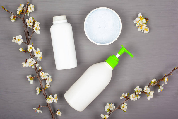 Vücut bakımı kozmetik ürünleri, gri arka planda beyaz şişeler, çiçek açan kiraz dalları, üst görünüm - Fotoğraf, Görsel