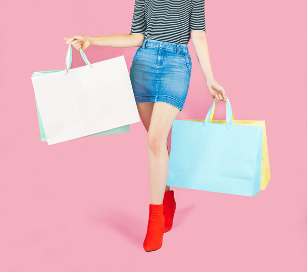 The female body part wore pink skirt jean and red boots. Carrying a shopping bag in many pastel colors on pink background selective focus,shopping concept - Φωτογραφία, εικόνα